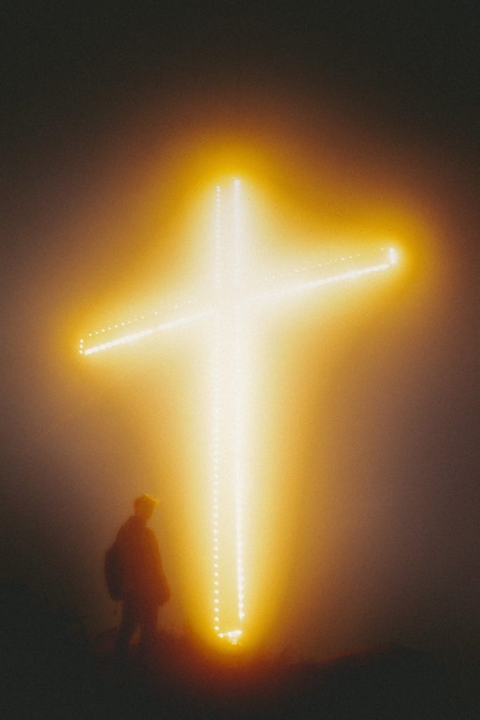 unrecognizable religious man against shiny cross at night